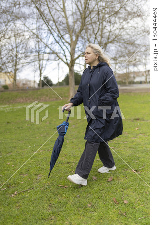 Woman walking in park with umbrella on cloudy day 130444469