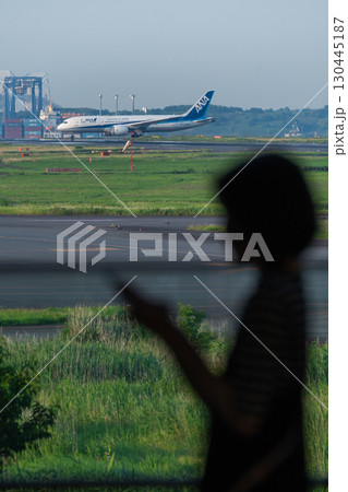 羽田空港の滑走路でまもなく離陸する飛行機と女性のシルエット 羽田空港の滑走路でまもなく離陸する飛行機と女性のシルエット 130445187