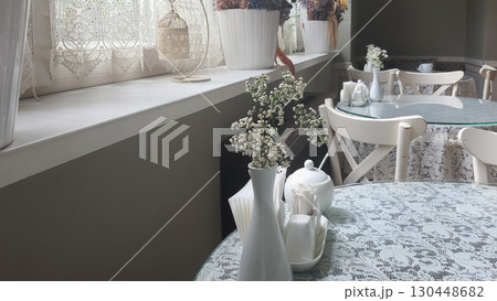 Cozy cafe setting with vintage decor and delicate floral arrangements in a sunlit room Cozy cafe setting with vintage decor and delicate floral arrangements in a sunlit room 130448682