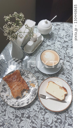 Enjoying a warm drink and dessert on a lace tablecloth in a cozy cafe setting 130448685