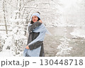 Joyful woman enjoying a snowy winter day by a tranquil river during the Christmas season 130448718