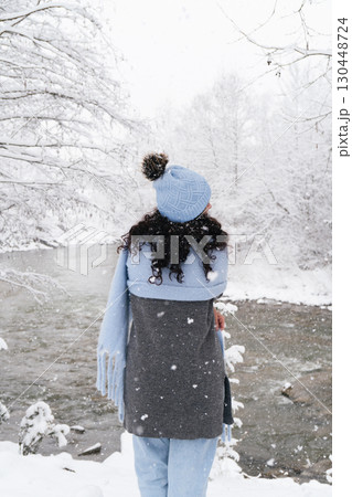 Joyful woman enjoying a snowy winter day by a serene river during the holiday season Joyful woman enjoying a snowy winter day by a serene river during the holiday season 130448724
