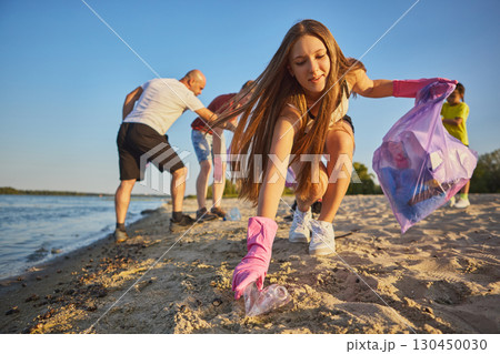Young woman in pink gloves cleaning beach near water with joyful emotion Young woman in pink gloves cleaning beach near water with joyful emotion 130450030