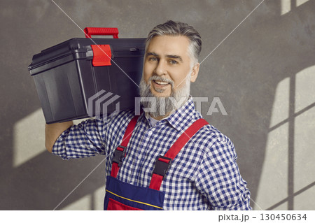 Portrait of a happy smiling mature bearded repairman holding a tool box isolated on gray background 130450634