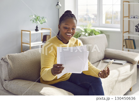 Happy woman sitting on the sofa at home and holding a business document and a mobile phone Happy woman sitting on the sofa at home and holding a business document and a mobile phone 130450636