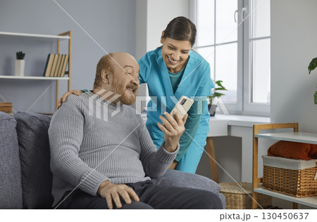 Young cheerful brunette nurse helping a senior patient how to use smartphone. Young cheerful brunette nurse helping a senior patient how to use smartphone. 130450637