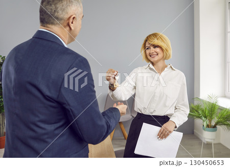 Smiling woman real estate agent gives the keys to a happy senior man house owner Smiling woman real estate agent gives the keys to a happy senior man house owner 130450653