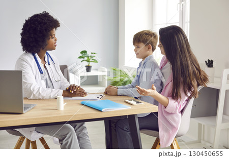 Female pediatrician talking to small boy patient and his mother in medical office 130450655