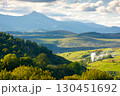 countryside landscape of transcarpathia on september evening. village in the valley and rural fields on the forested hills. carpathian mountain ridge with pikui peak in the distance 130451692