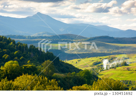 countryside landscape of transcarpathia on september evening. village in the valley and rural fields on the forested hills. carpathian mountain ridge with pikui peak in the distance 130451692