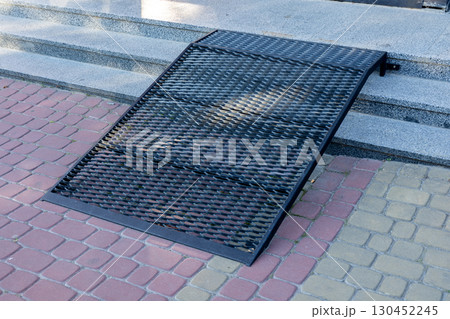 A black metal ramp rests against a staircase, providing accessibility for individuals with mobility challenges in an urban environment A black metal ramp rests against a staircase, providing accessibility for individuals with mobility challenges in an urban environment 130452245