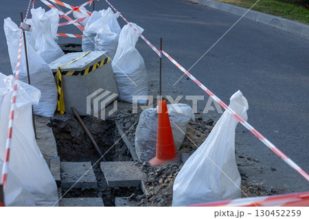 Roadwork in a city area with construction barriers, bags of materials, and an uncovered trench creating a temporary blockage Roadwork in a city area with construction barriers, bags of materials, and an uncovered trench creating a temporary blockage 130452259