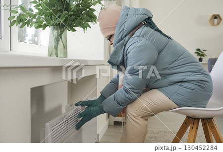 Frozen older woman feels very cold in apartment due to problems with heating. 130452284