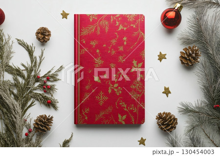 Red notebook with gold Christmas pattern surrounded by pine branches, pine cones and Christmas baubles on white background, perfect mockup for holiday greetings 130454003