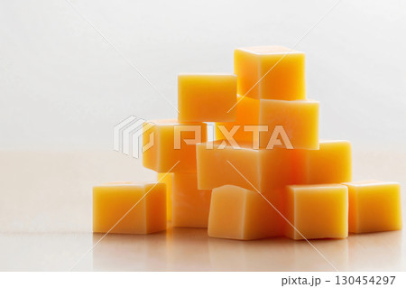 Bright yellow cheddar cheese cubes stacked on shiny surface, isolated on white background with wooden table backdrop. Delicious and nutritious snack ingredient 130454297