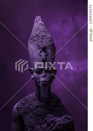 Stone statue of Osiris, the ancient Egyptian god of the underworld and resurrection, standing against a purple background with smoke 130454575