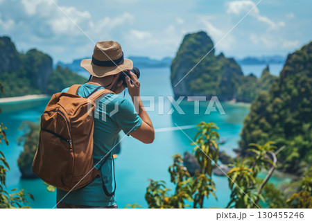 Photographer is capturing the beauty of a tropical island with his camera, standing on a cliff overlooking the turquoise waters 130455246