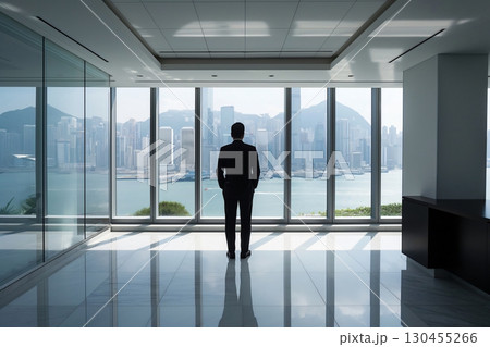 Businessman standing in a modern office, looking out at the impressive skyline of hong kong Businessman standing in a modern office, looking out at the impressive skyline of hong kong 130455266