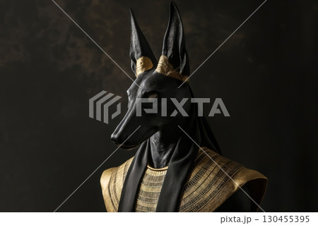 Black jackal god anubis statue wearing a golden headband is looking down with a dark background 130455395