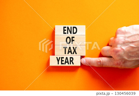 End of tax year symbol. Concept words phrase End of tax year on beautiful wooden blocks. Beautiful orange paper background. Businessman's hand. Business End of tax year concept. Copy space. 130456039