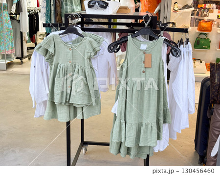 Green cotton kids dresses on hangers in a clothing store. Fashion, textile design, seasonal wardrobe and retail shopping in casual summer style. 130456460