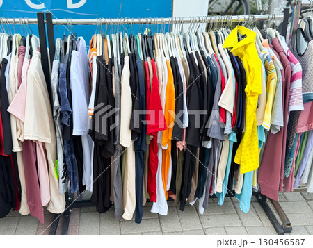 Close view of colorful t-shirts hanging in street retail market. Shopping, fashion, and lifestyle consumer concept in outdoor commerce. 130456587
