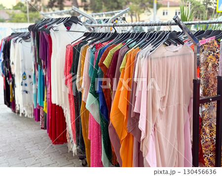 Clothing rack with colorful dresses displayed in street market. Retail, shopping, and fashion concept in outdoor urban commerce environment. Clothing rack with colorful dresses displayed in street market. Retail, shopping, and fashion concept in outdoor urban commerce environment. 130456636