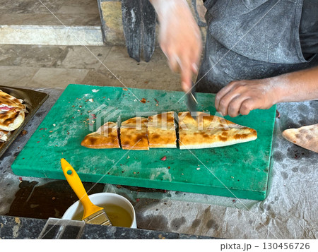 Chief Baked cuts flatbread on a table. Traditional cuisine, handmade preparation and authentic food culture. Chief Baked cuts flatbread on a table. Traditional cuisine, handmade preparation and authentic food culture. 130456726