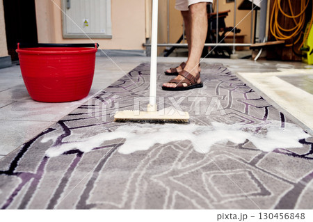 Man Cleaning a Rug with a Brush and Soapy Water 130456848