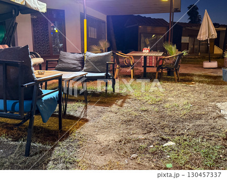 Outdoor cafe terrace with tables, chairs and sofas illuminated in the evening. Hospitality, leisure, service, social environment and comfort in a night setting. 130457337