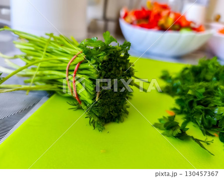 A fresh bundle of parsley with stems and leaves on a green cutting board, prepared in the kitchen for use in salads, soups, and other homemade healthy dishes with natural ingredients. 130457367
