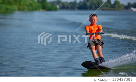 Boy wakeboarding smoothly on calm lake with serious concentration 130457395