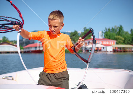 Boy in orange shirt preparing wakeboarding rope on boat with focus Boy in orange shirt preparing wakeboarding rope on boat with focus 130457399