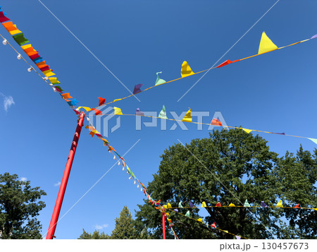 Colorful party flags hang across the sky, creating a vibrant, festive atmosphere for outdoor events. The clear blue sky and lush trees in the background add to the cheerful celebration Colorful party flags hang across the sky, creating a vibrant, festive atmosphere for outdoor events. The clear blue sky and lush trees in the background add to the cheerful celebration 130457673