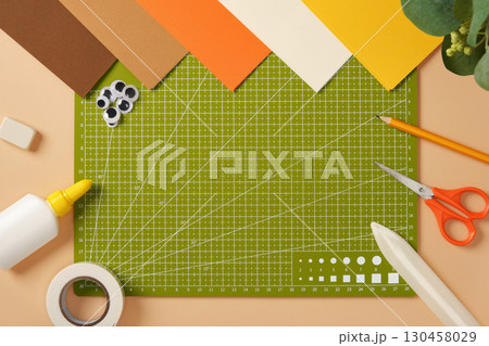 Green cutting mat surrounded by colored paper and crafting tools on a table. Creative workspace for arts and crafts. Green cutting mat surrounded by colored paper and crafting tools on a table. Creative workspace for arts and crafts. 130458029