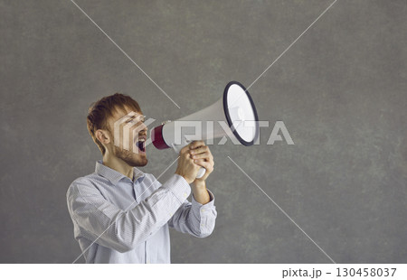 Man holding a megaphone and making an announcement isolated on a grey background Man holding a megaphone and making an announcement isolated on a grey background 130458037