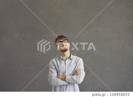 Portrait of a serious caucasian young man with a pensive expression on a gray background. 130458055