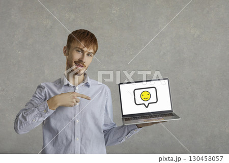 Happy young man pointing at a smiling emoticon on the screen of his laptop computer Happy young man pointing at a smiling emoticon on the screen of his laptop computer 130458057