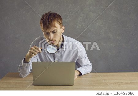 Young handsome man looks through a magnifying glass 130458060