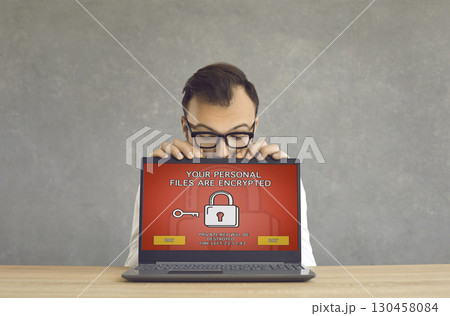 Man gets his laptop computer hacked and receives a ransomware warning on the screen 130458084