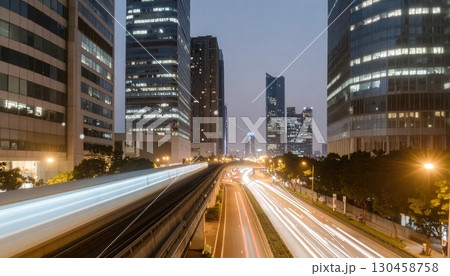Vibrant cityscape at dusk featu illuminated skyscrapers modern high-rise office buildings and a busy highway with light trails in an urban environment 130458758