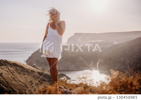 A blonde woman stands on a hill overlooking the ocean. She is wearing a white dress and she is enjoying the view. A blonde woman stands on a hill overlooking the ocean. She is wearing a white dress and she is enjoying the view. 130458965