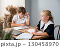 Children Studying Homework Classroom - Two children in school uniforms are seated at a table, working on their homework in a classroom. 130458970