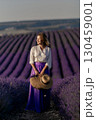 A woman wearing a purple skirt and a straw hat stands in a field of lavender 130459001