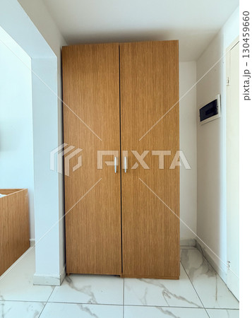 Wooden wardrobe in a modern room interior with tiled floor and minimalistic design. Storage, functionality and organization as part of everyday lifestyle and domestic environment. Wooden wardrobe in a modern room interior with tiled floor and minimalistic design. Storage, functionality and organization as part of everyday lifestyle and domestic environment. 130459660