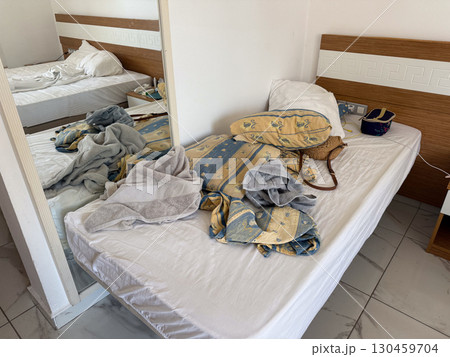 Hotel room interior with two beds, mirror, and daily belongings scattered on sheets, messy room. Accommodation, hospitality, lifestyle, rest and everyday travel environment. 130459704
