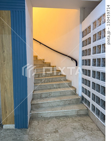 Marble staircase with handrail illuminated by yellow light inside a building. Architecture, construction, passage, interior design and functional indoor environment. Marble staircase with handrail illuminated by yellow light inside a building. Architecture, construction, passage, interior design and functional indoor environment. 130459714