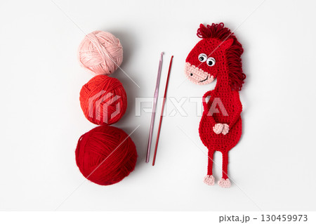 Crocheted toy fiery red horse and three red and pink balls with a crochet hook on a gray background. The symbol of the year 2026. Chinese New Year greeting card 130459973