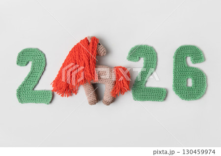 Crocheted toy fiery red horse and green numbers. The symbol of the year 2026 on a gray background. Chinese New Year greeting card Crocheted toy fiery red horse and green numbers. The symbol of the year 2026 on a gray background. Chinese New Year greeting card 130459974