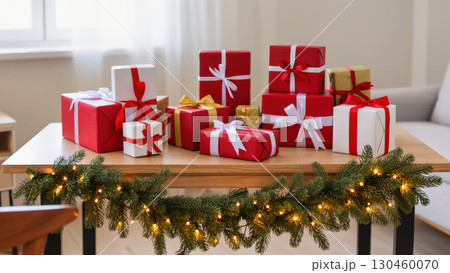 Christmas presents wrapped in red, white, and gold paper with ribbons on wooden table decorated with garland and lights. Festive holiday indoor scene. 130460070